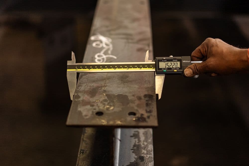A worker measuring a steel part with a digital caliper.